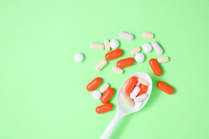 Top view of plastic spoon with pills and vitamins on green table with copy space