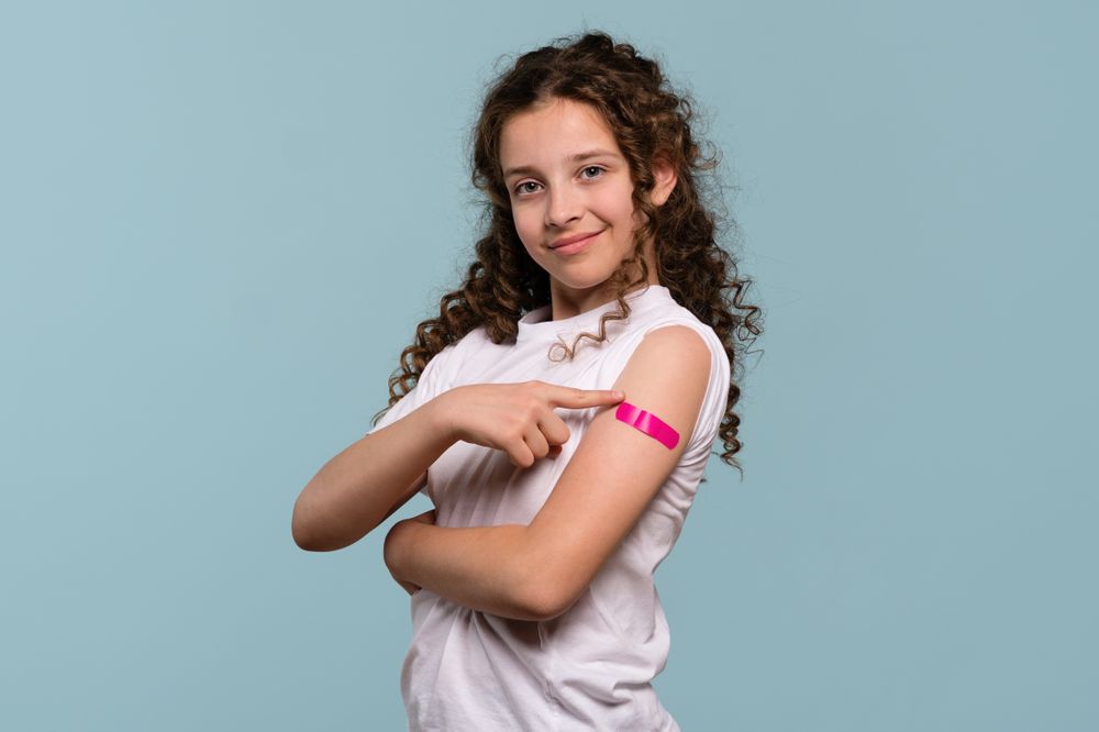 Girl pointing at pink bandage on arm after receiving vaccine.