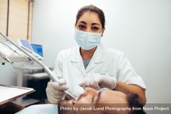 Female dentist wearing face mask looking at camera while treating a patient 0LDJr0