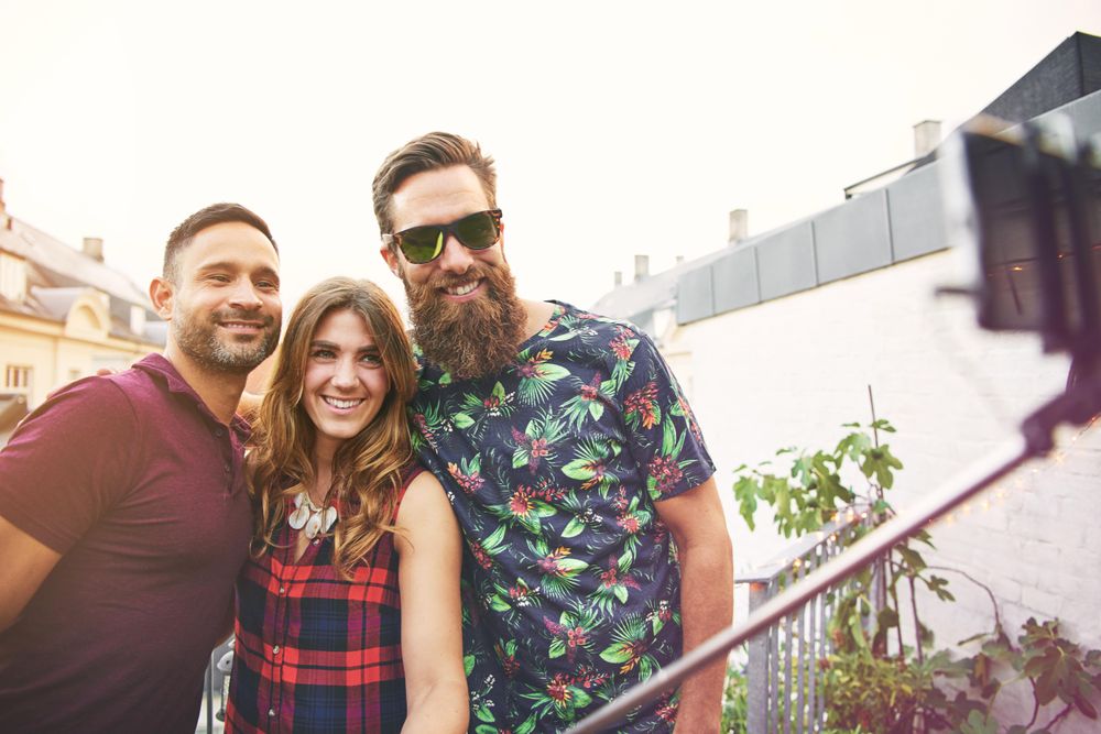 Group of smiling friends with selfie stick on roof