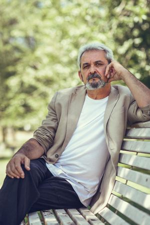 Portrait of a grey haired man, sitting on bench in a park