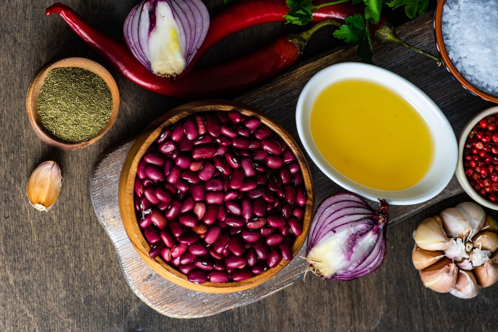 Top view of bowls of kidney beans, oil, pepper, garlic bulb and onions