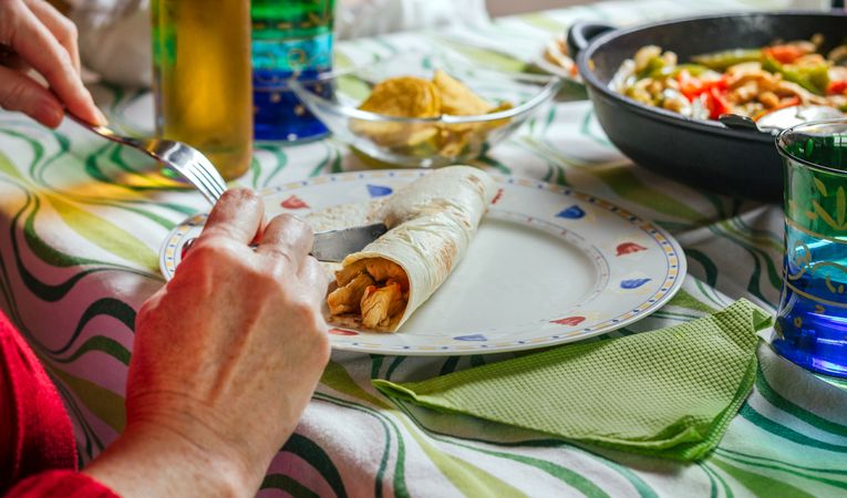 Woman rolling mexican fajita on the plate