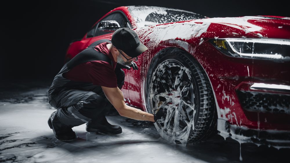 Red Sportscar's Wheels Covered in Shampoo Being Rubbed by a Soft Sponge at a Stylish Dealership Car Wash.