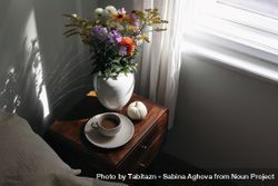 Cup of coffee, pumpkin on wooden bedside table with vase in sunlight 0Lz8e4