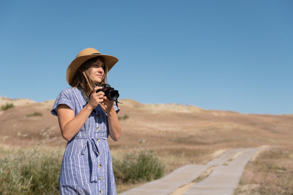 adult woman in straw hat and dress with camera standing on country path