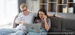 Laughing couple talking and looking on laptop together in the living room 0L9Rr5