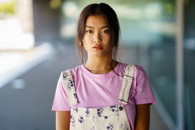 Chinese female in floral overalls and pink t-shirt looking at camera outside