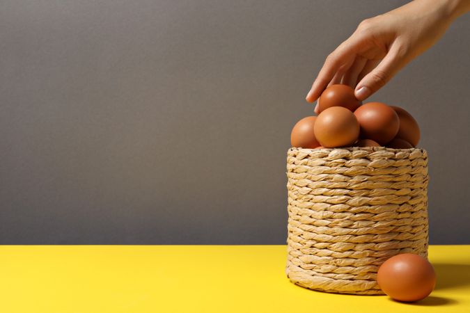 Eggs in a wicker basket, with a hand, on a gray background.