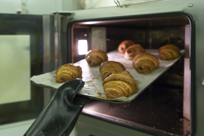 Cook holding baking tray with hot croissants
