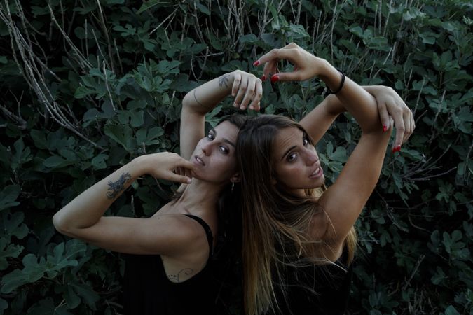 Young women posing near green bush
