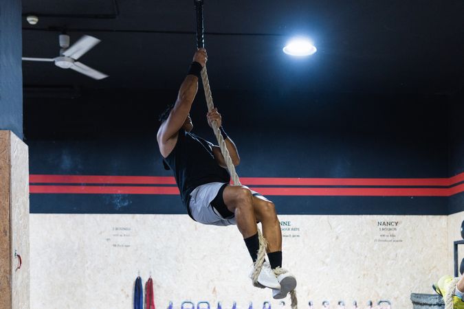 Strong sportsman exercising on climbing rope