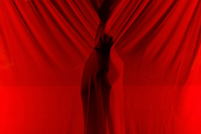 Faceless person hiding behind curtains at night time