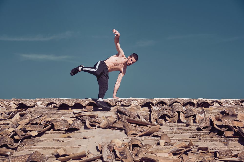 Athletic man performing handstand rotation while dancing breakdance on roof