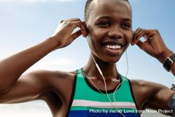 Close up of smiling female runner adjusting her earphones during a workout break beNXE0