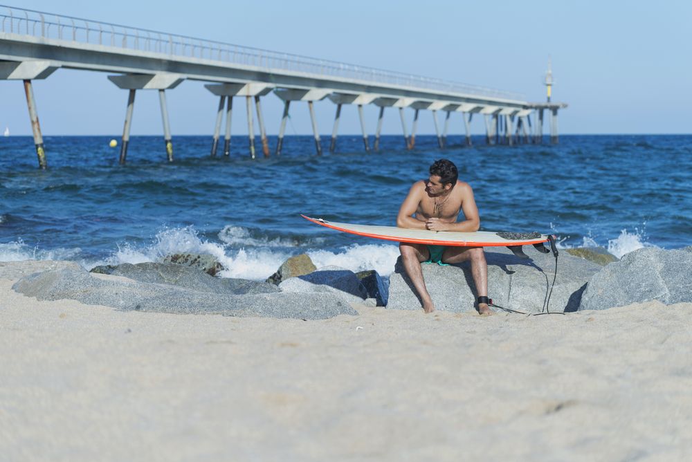 Male surfer relaxing near ocean with board on lap