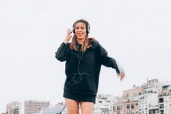 Content young woman in casual wear dancing while using headphones at city street