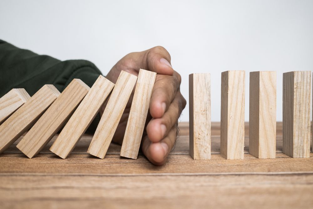 male hand stop falling wooden blocks. domino effect or risk protection strategy concept