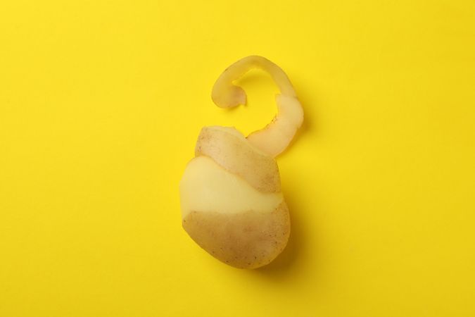Partially peeled potato on yellow background