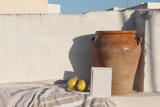 Blank greeting card, invitation mock up in sunlight leaning on vintage olive clay pot and fresh lemons fruit