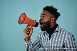 Portrait of a Black man in blue studio shoot yelling into megaphone bGndv4