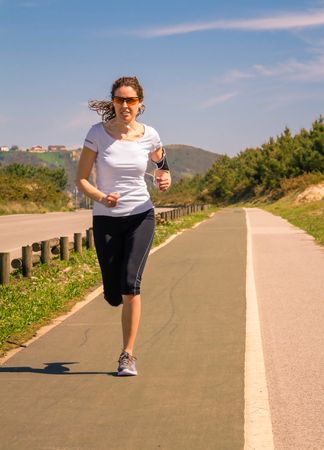 Woman in athletic gear jogging along road, vertical