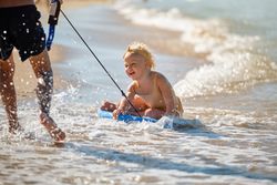 Cheerful toddler sitting on surfboard on beach