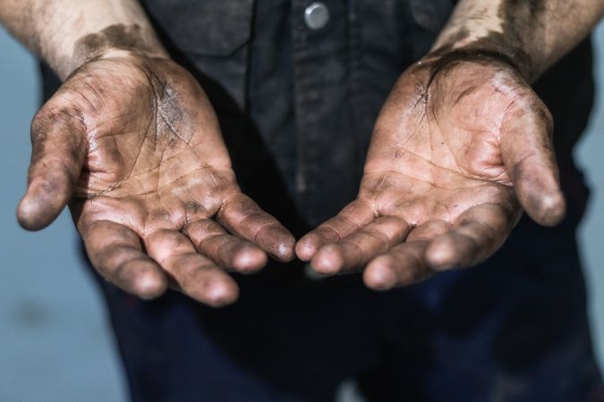 Mechanic showing dirty hands in car workshop