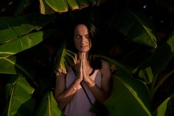 Peaceful Hispanic woman with prayer hands near green trees