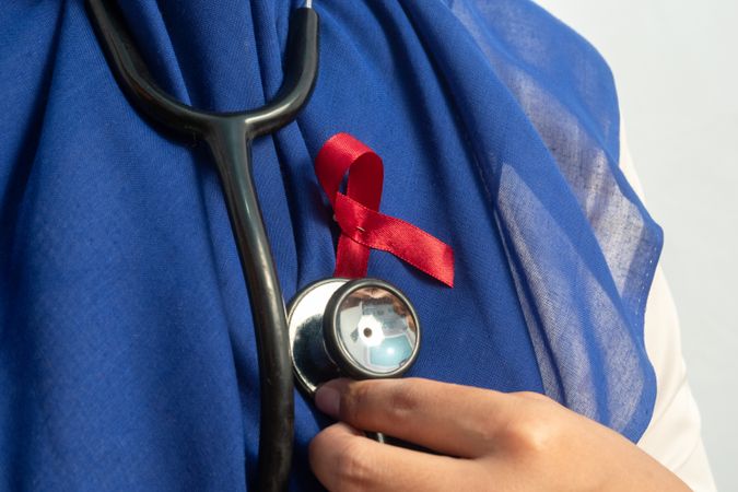 Happy Muslim Female Asian doctor or nurse with Red ribbons and stethoscope, HIV awareness concept, world AIDS day, world cancer day.