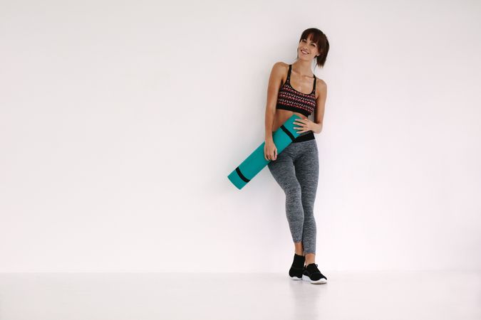 Smiling woman with yoga mat in studio