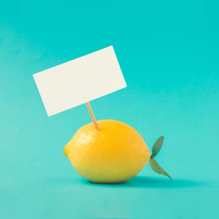Lemon with paper card note on bright blue background