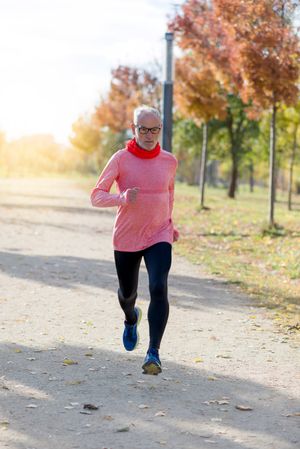 Mature man jogging outside in sunny park