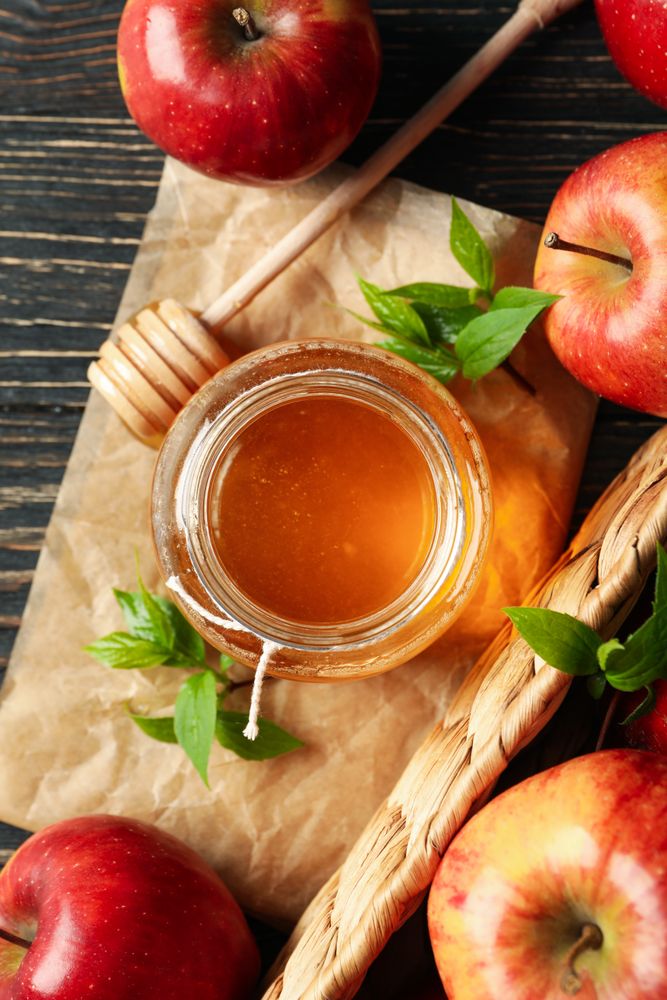 Looking down at pot of honey with dipper and apples, vertical