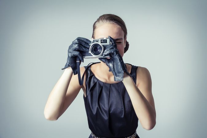 Model in chic clothing and gloves taking selfie with vintage camera