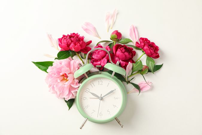 Flat lay composition with beautiful peonies and alarm clock on plain background, space for text