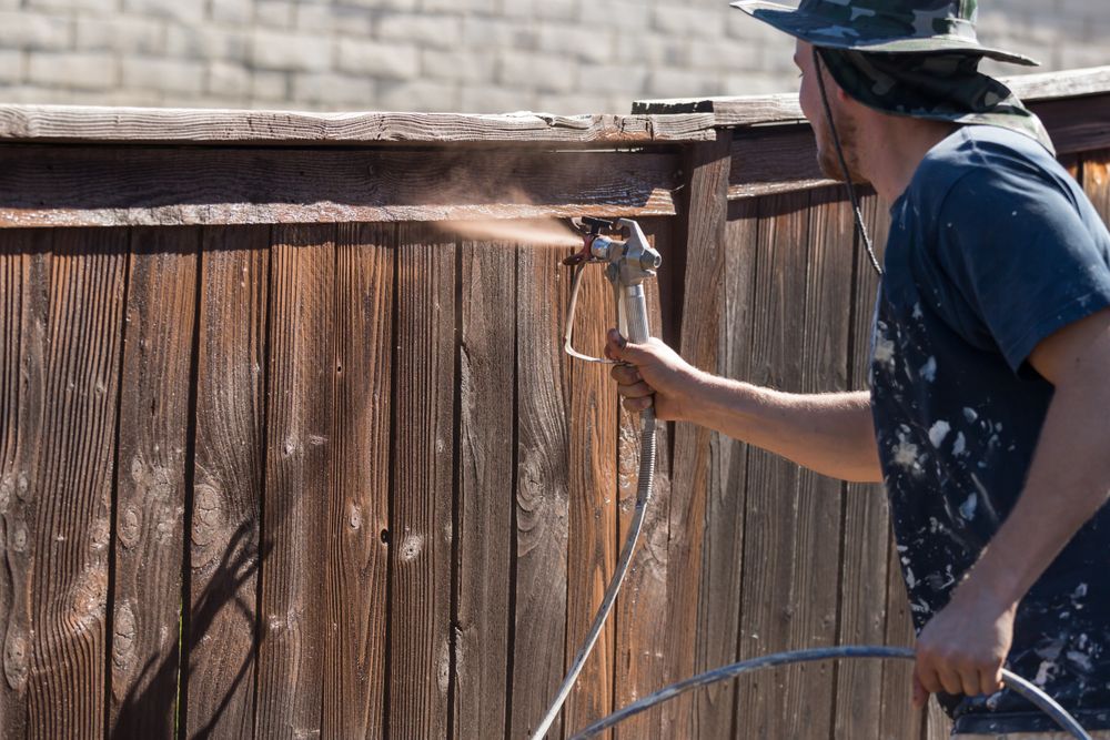 Professional Painter Spraying Yard Fence with Stain