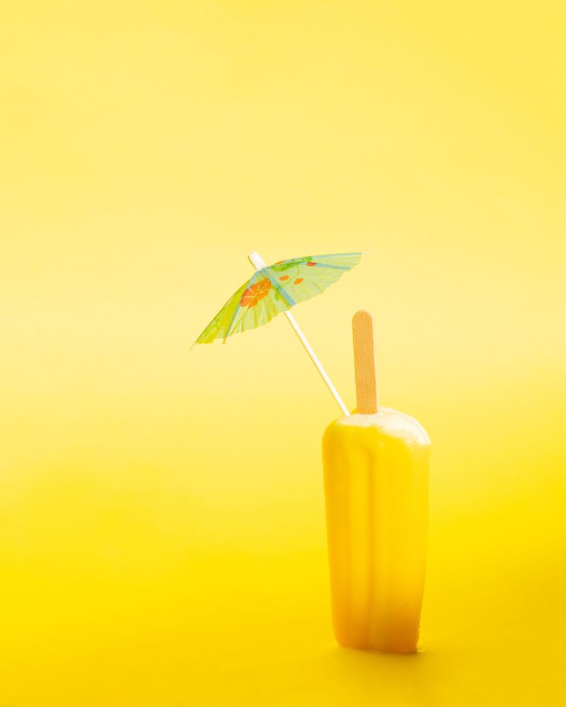 Ice pop with cocktail parasol on yellow background