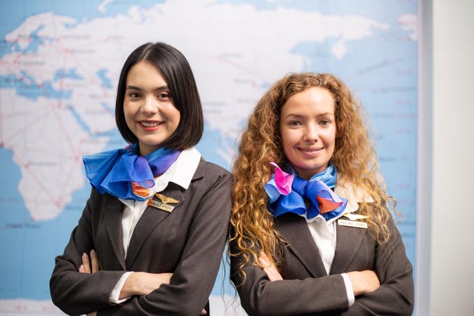 Two female flight attendants standing in front of map and smiling