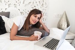 Woman lounging in bed with coffee and laptop