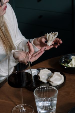 Cropped image of blonde woman sitting at a dinner table eating dumpling