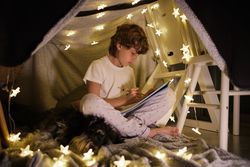 Focused boy drawing in blanket fort at home
