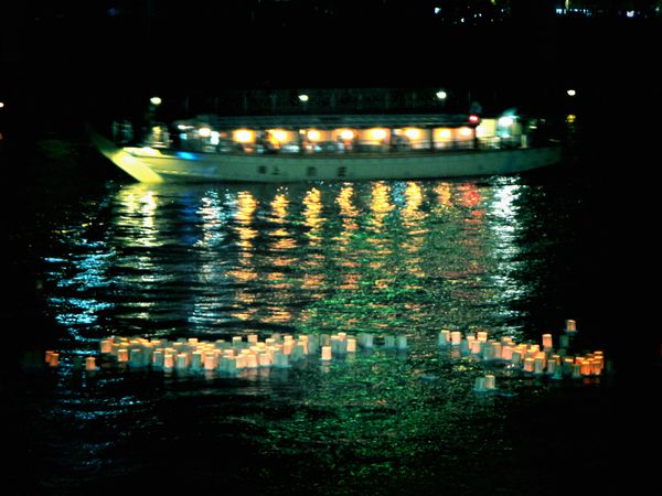 Lit lanterns floating on water near boat at night