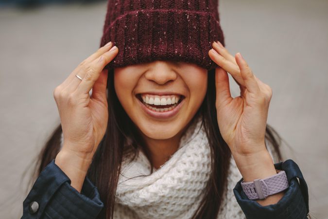 Woman pulling knit cap down over eyes and smiling