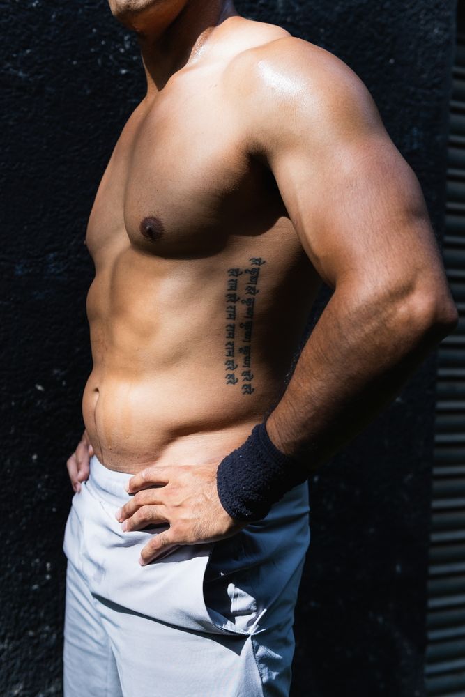 Anonymous positive shirtless Hispanic sportsman near wall