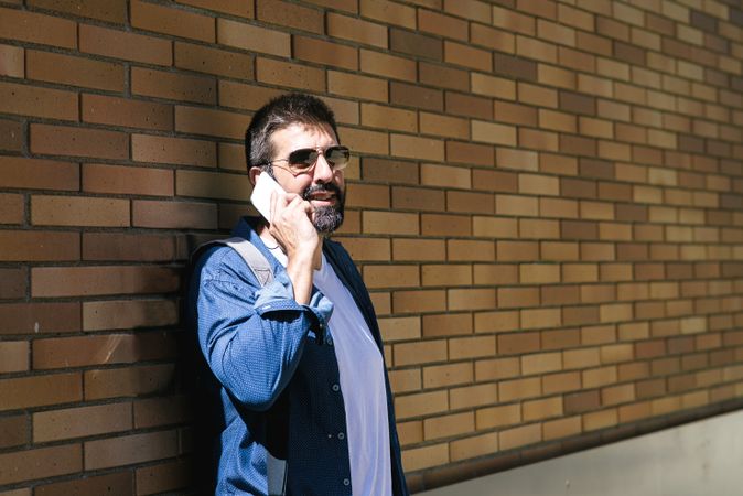 Man leaning on brick wall chatting on phone