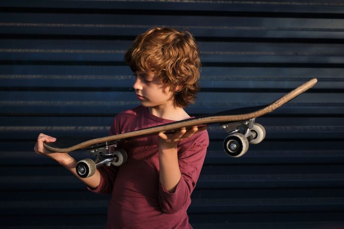 Boy checking skateboard against blue wall