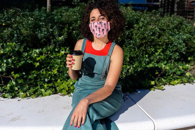 Woman with afro hair is sitting outside on a sunny day wearing a medical mask