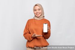 Happy Muslim woman smiling presenting smart phone with mock up screen 4NLDe0
