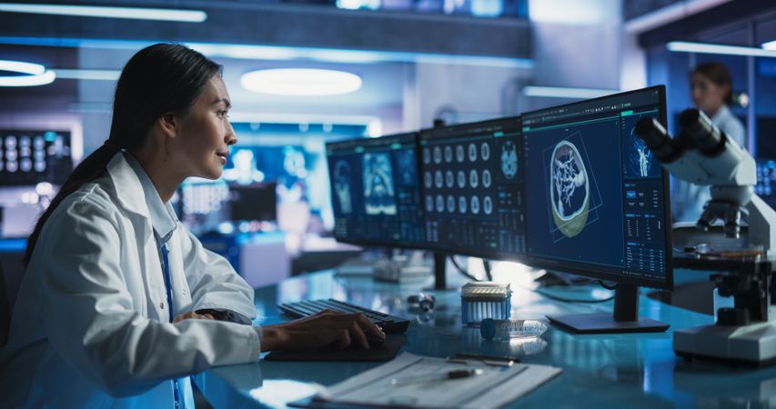 Female Asian Neuroscientist Using Desktop Computer With Human Brain CT Scans In Modern Medical Research Center Laboratory.